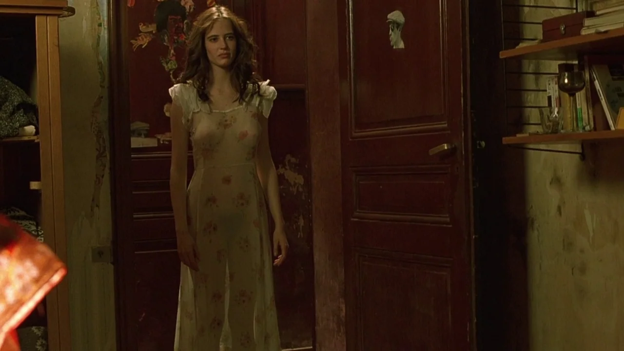 The Dreamers (2003) movie still: fullbody — An interior space features dark wood doors and worn, textured walls. A woman stands centered in the…