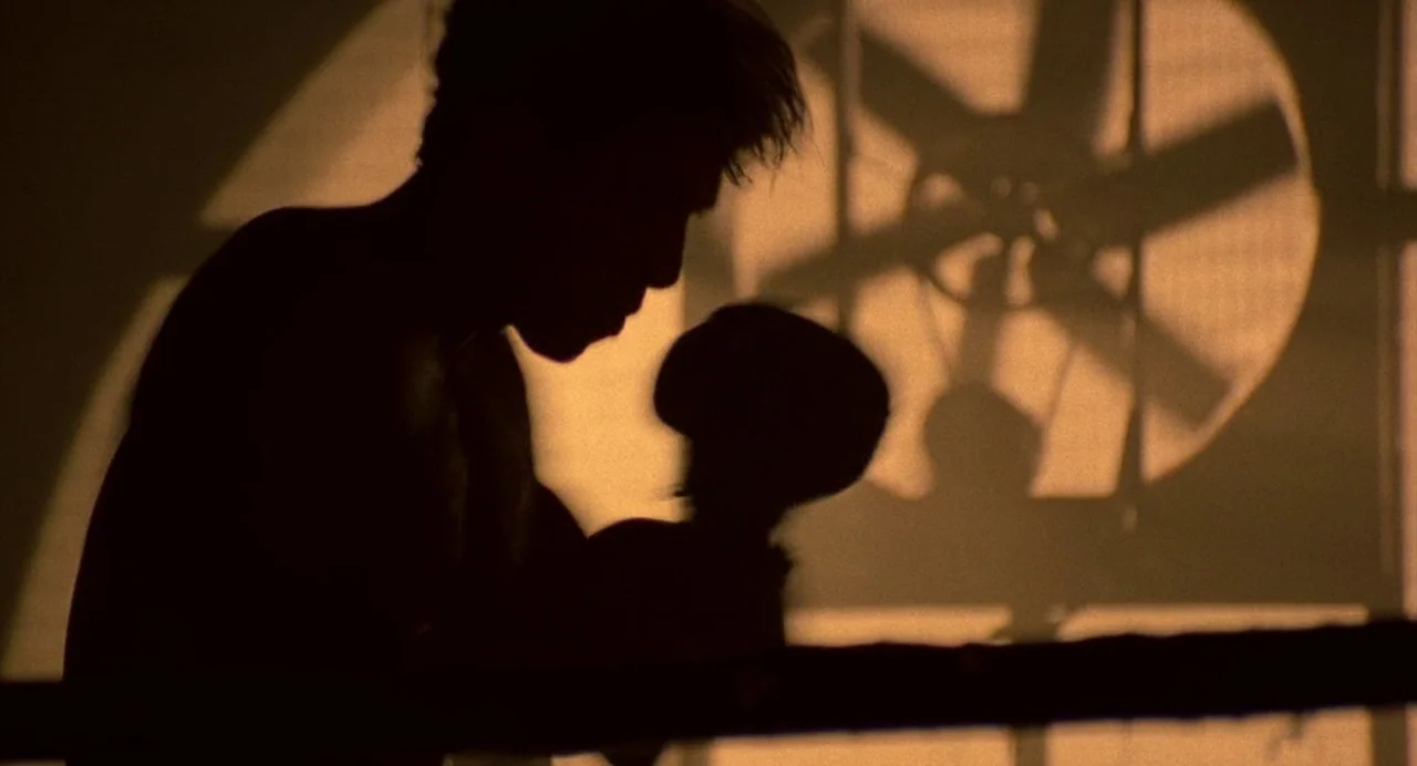 Bad Boys (1995) movie still: medium — A dimly lit room contains a silhouette of a man by a fan. The man leans forward against a rope with a large…