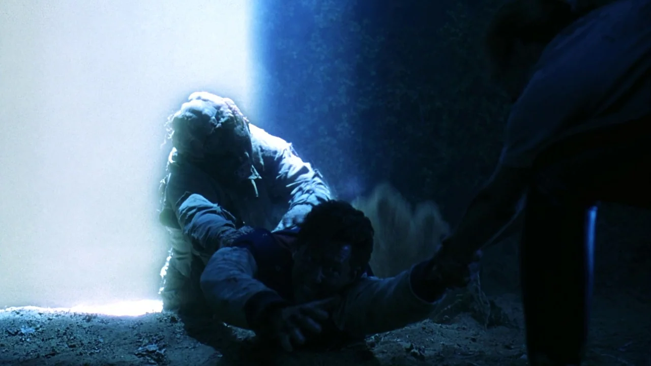 Jason Goes To Hell (1993) movie still: medium — A man is being dragged across the dark dirt ground by an assailant. A bright white light illuminates…