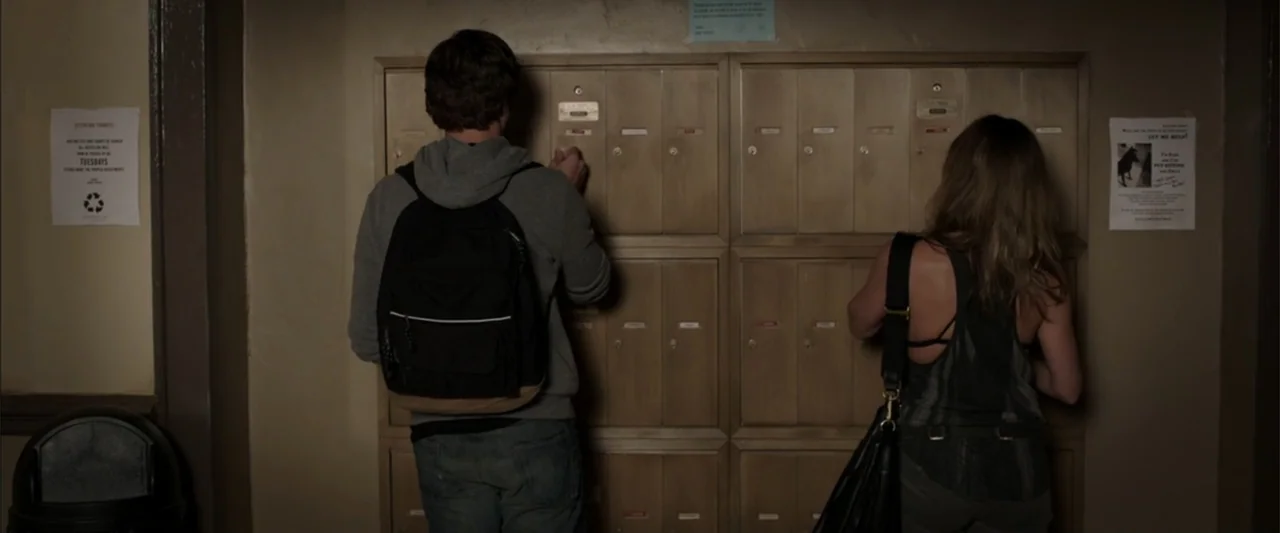 We're the Millers (2013) movie still: medium — A dimly lit interior apartment mailroom features two rows of beige metal mailboxes. A young man and…