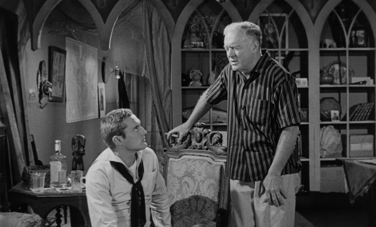 Night Tide (1961) movie still: medium — An interior study with arched bookshelves containing various curios and a nautical map. An older man stands…