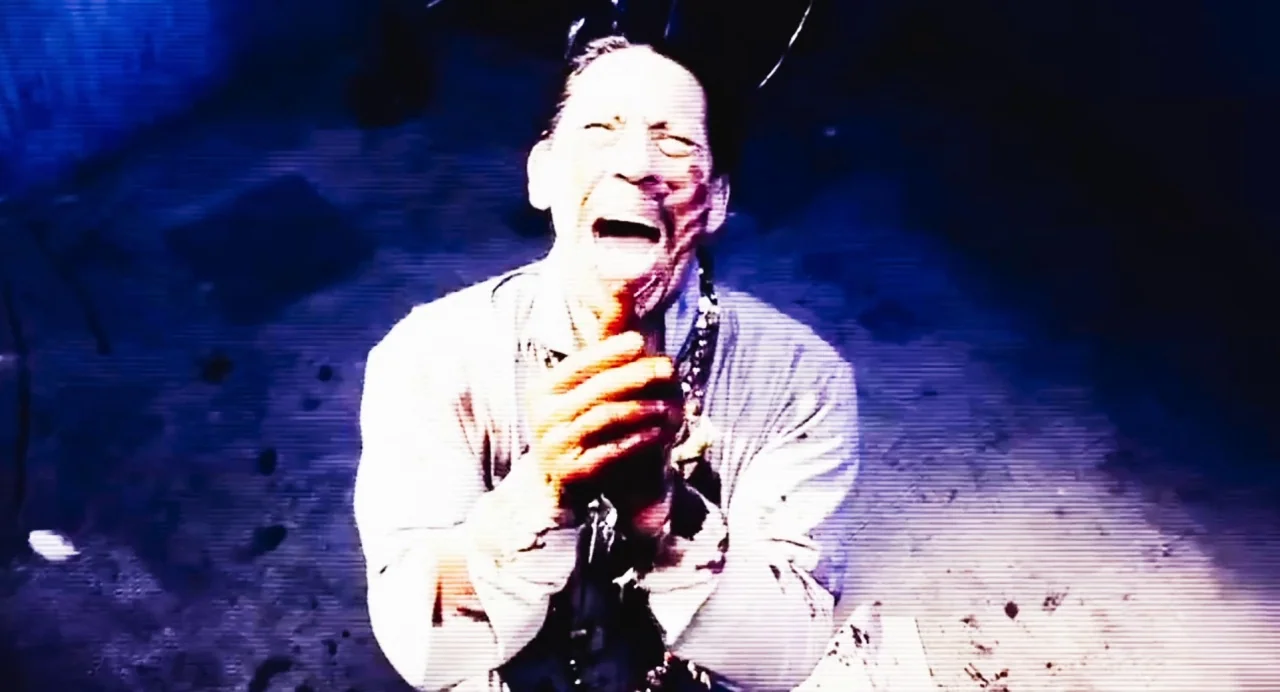 Zombi Child (2019) movie still: medium — A dimly lit enclosed space with a rough floor and deep blue shadows. A man with his head tilted back…