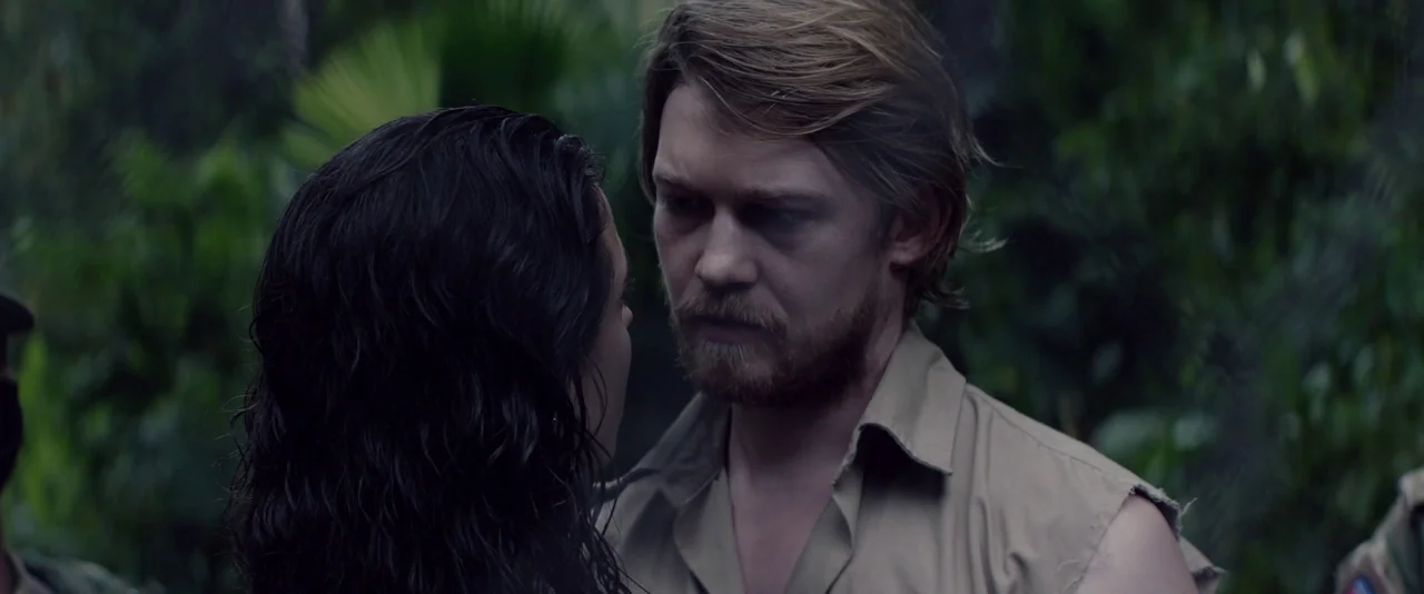 Stars At Noon (2022) movie still: medium — A man and woman stand close together in a dark, humid, overgrown tropical environment. The woman has wet…