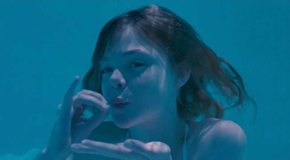 Somewhere (2010) movie still: closeup — A person is submerged in a large body of blue water. The subject is seen from the chest up while making a…