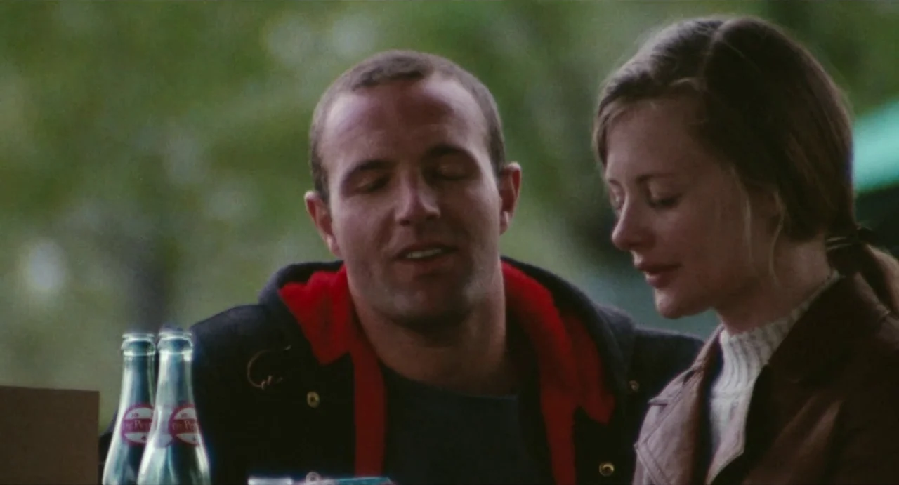 The Rain People (1969) movie still: medium — A man and woman sit together at a table in a park setting. They are positioned side by side as they…
