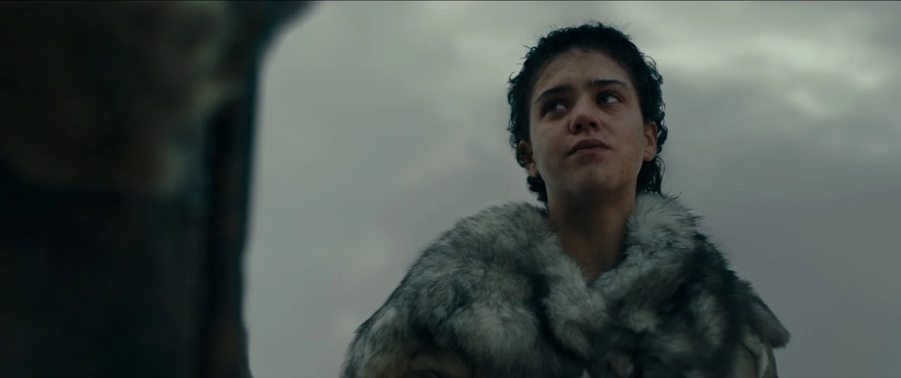 Out of Darkness (2022) movie still: medium — An open and overcast tundra landscape serves as the backdrop for the character. The woman stands…