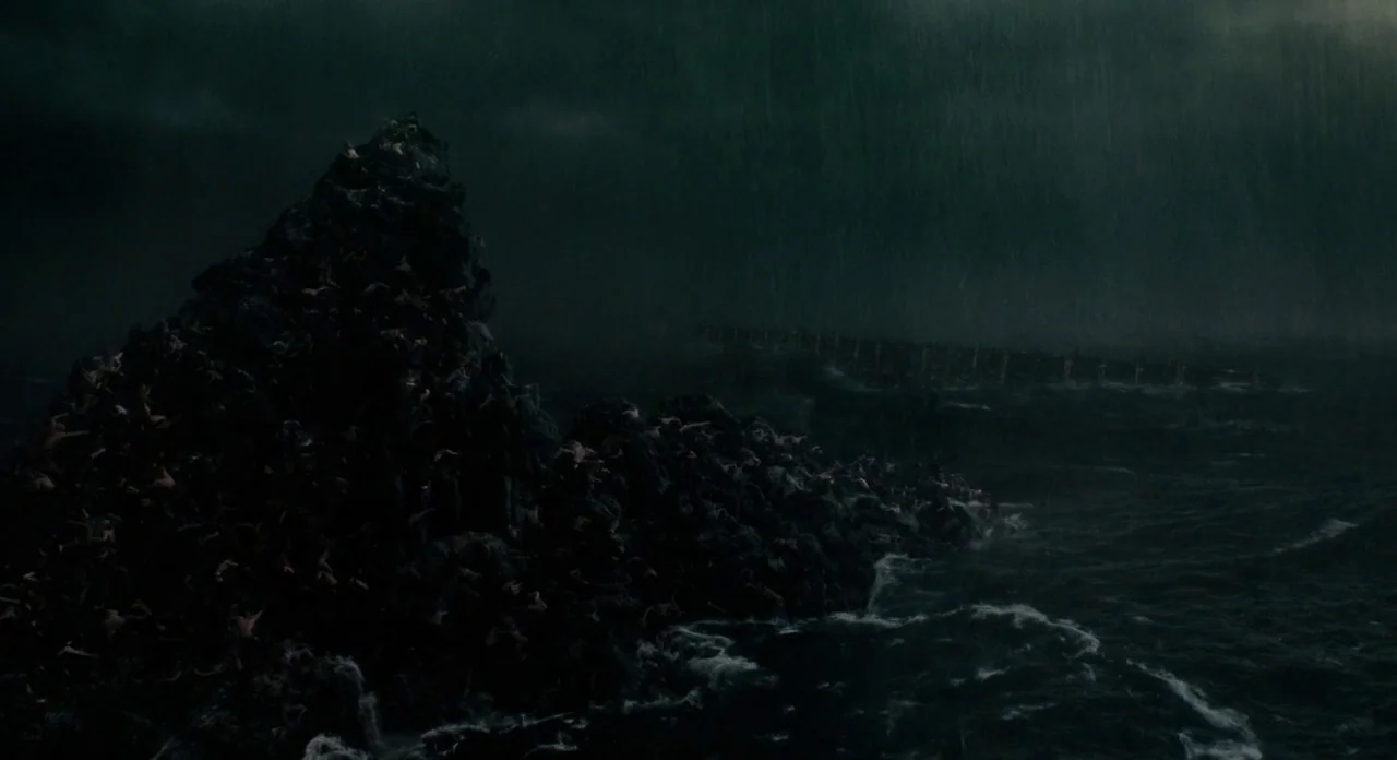 Noah (2014) movie still: establishing — A dark, storm-lashed ocean crashes against a large, jagged rock formation at night. Rain pours over the…
