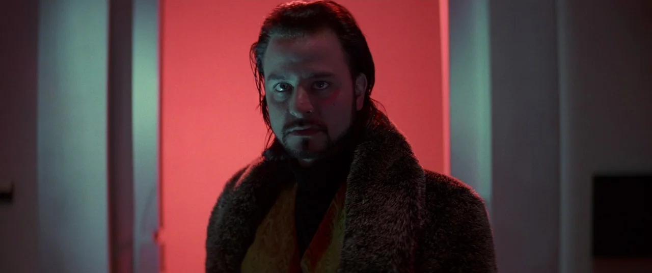 Hackers (1995) movie still: medium — A man stands centered within a doorway illuminated by bright red light from behind. He gazes forward while dark…