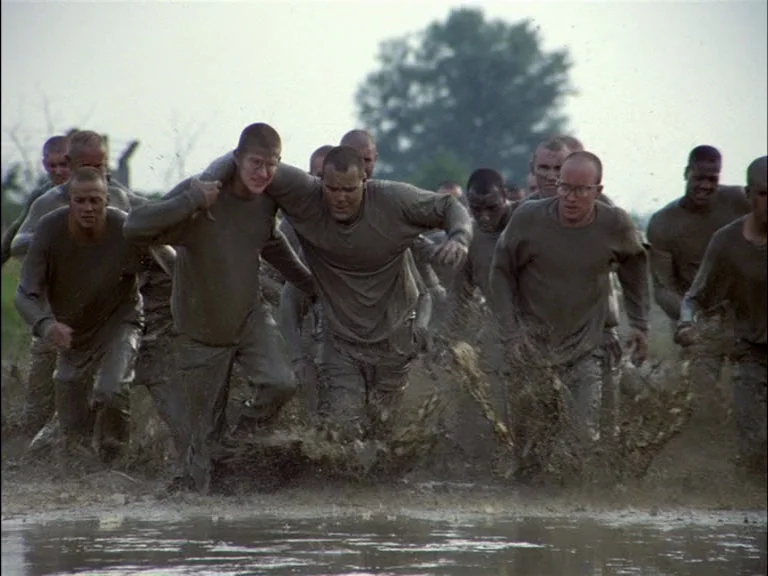 Full Metal Jacket (1987) movie still: fullbody — A group of military recruits runs through deep, murky mud during outdoor training exercises. One…