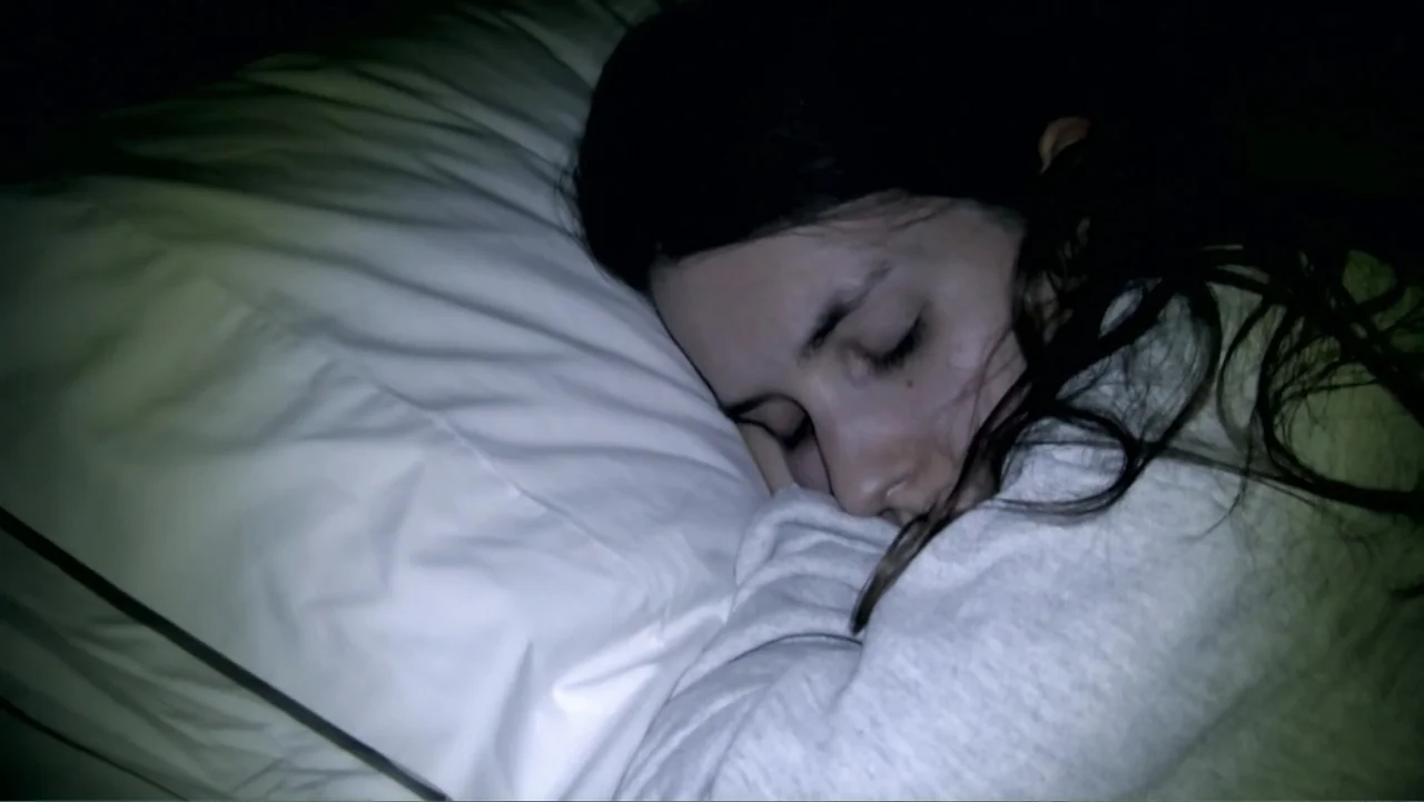 S-V/H/S: Un cortometraje de Las Crónicas del Miedo (2023) movie still: closeup — A dark, dimly lit bedroom at night with a person asleep on a…