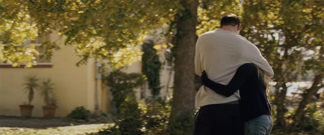 Dear John (2010) movie still: medium — A man and woman embrace in a yard in front of a yellow house. The scene is illuminated by warm, dappled…