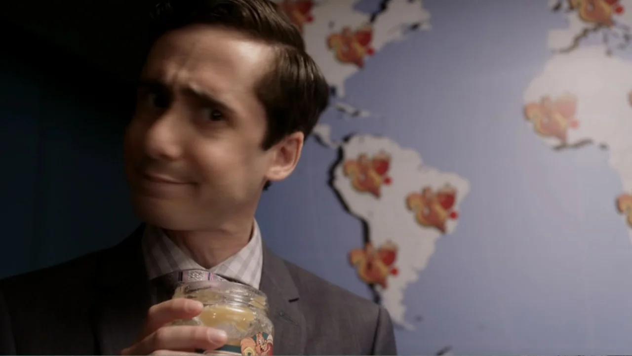 Rufus 2 (2017) movie still: medium — A professional office space features a wall decorated with a stylized map graphic. A young man in a suit holds…