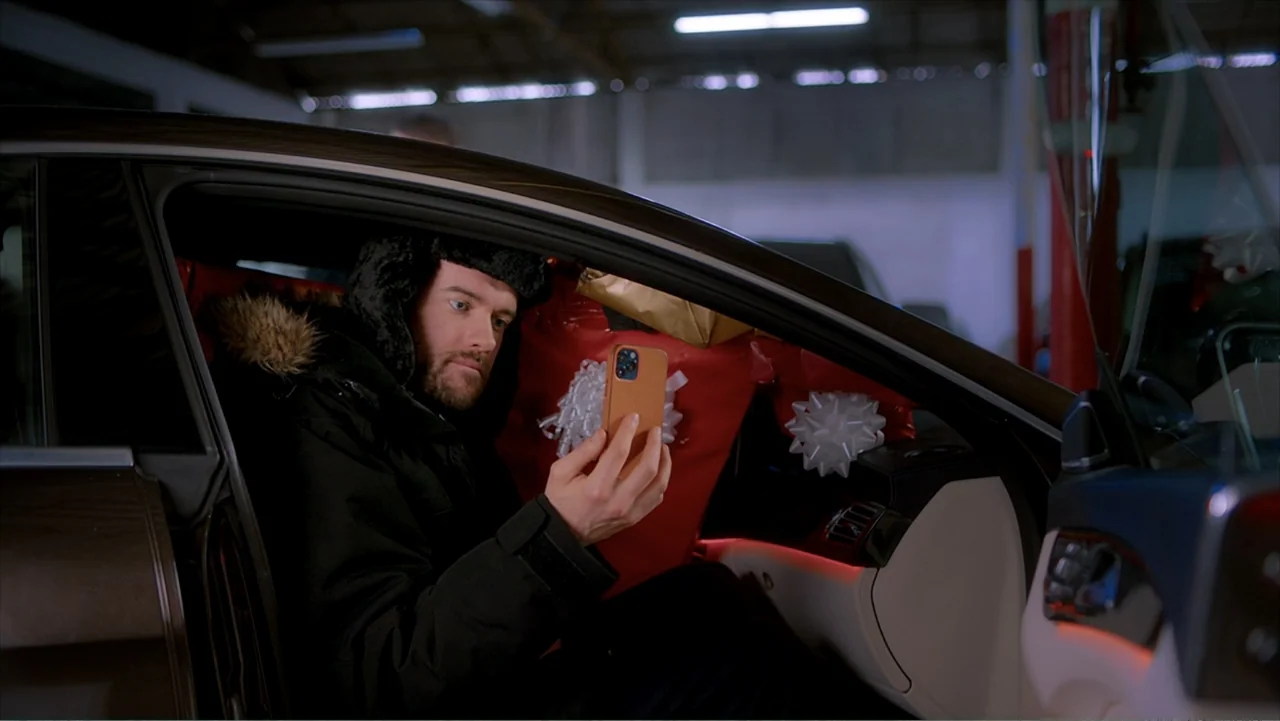 Jack in Time for Christmas (2024) movie still: medium — A man sits in the driver seat of a dark luxury car with red gift wrapping inside. He holds a…