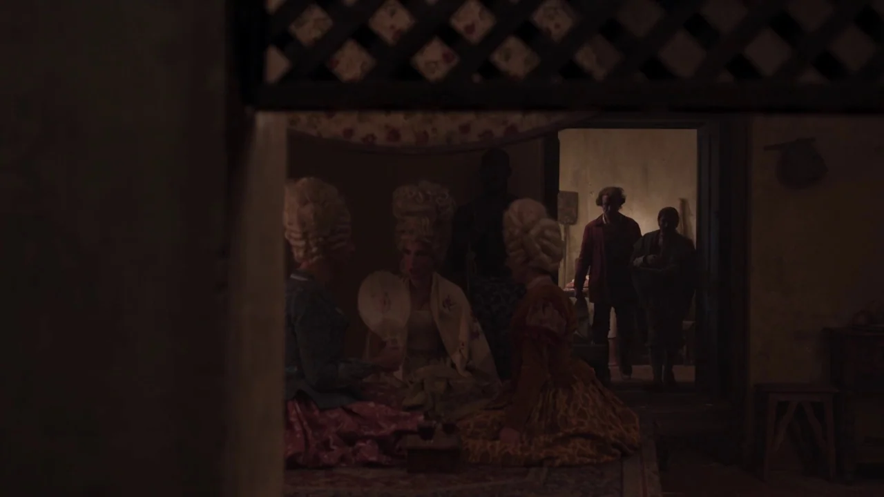 Zama (2017) movie still: wide — A dimly lit room features women in white wigs sitting on the floor together. Two men enter the space from an…
