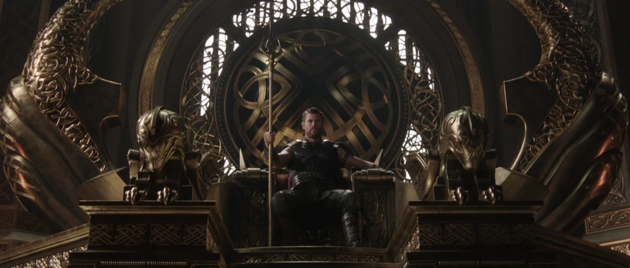 Thor: Ragnarok (2017) movie still: fullbody — A high-backed gold throne sits in front of a massive circular ornamental window. A man in dark armor…