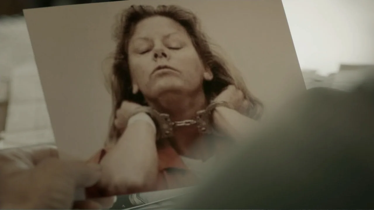 Aileen Wuornos : Mind of a Monster (2020) movie still: closeup — A hand holds a physical photograph depicting a woman in custody. The woman in the…