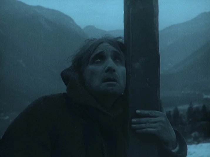 Making of: The Wheel (La Roue) (1923) movie still: closeup — A man stands outdoors in a mountainous region under a dark, overcast blue sky. He leans…
