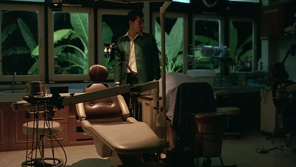 Syndromes and a Century (2006) movie still: medium — A dimly lit dental clinic features a vintage chair surrounded by specialized metal equipment. A…