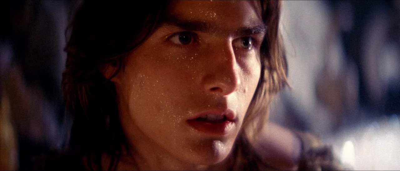 Legend (1985) movie still: closeup — A dark, dimly lit environment features a person with sparkling dust on their face. The subject stares ahead…
