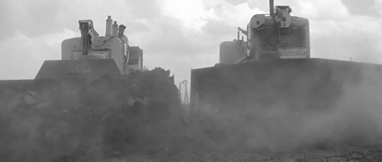 Hud (1963) movie still: wide — Two heavy duty bulldozers move mounds of dark soil across a wide open field. A man operates each vehicle while…