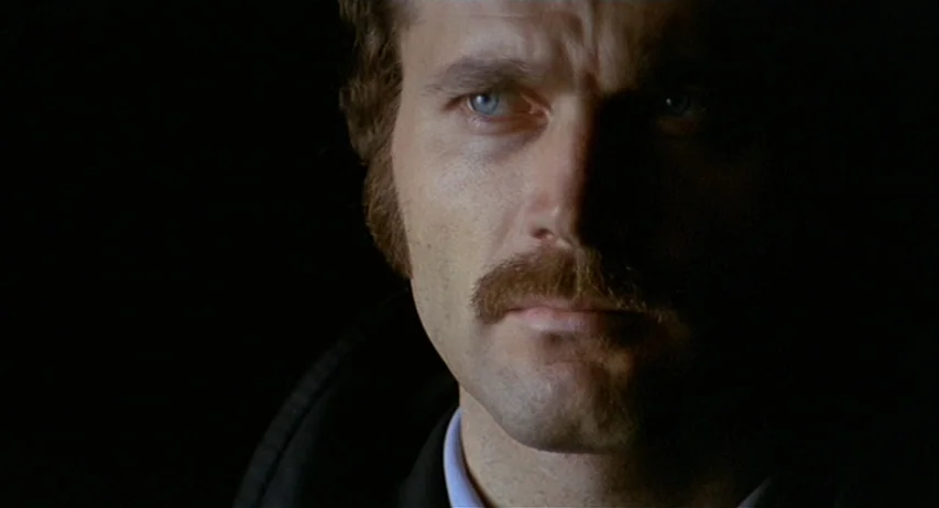 The Fifth Cord (1971) movie still: closeup — A man's face is illuminated from one side against a pitch-black background. He stares straight ahead…