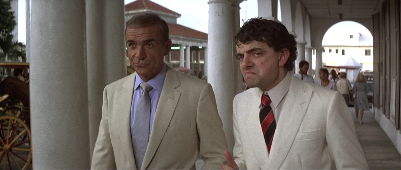 Never Say Never Again (1983) movie still: medium — A stone-columned exterior walkway features archways and a distant white building. Two men in…