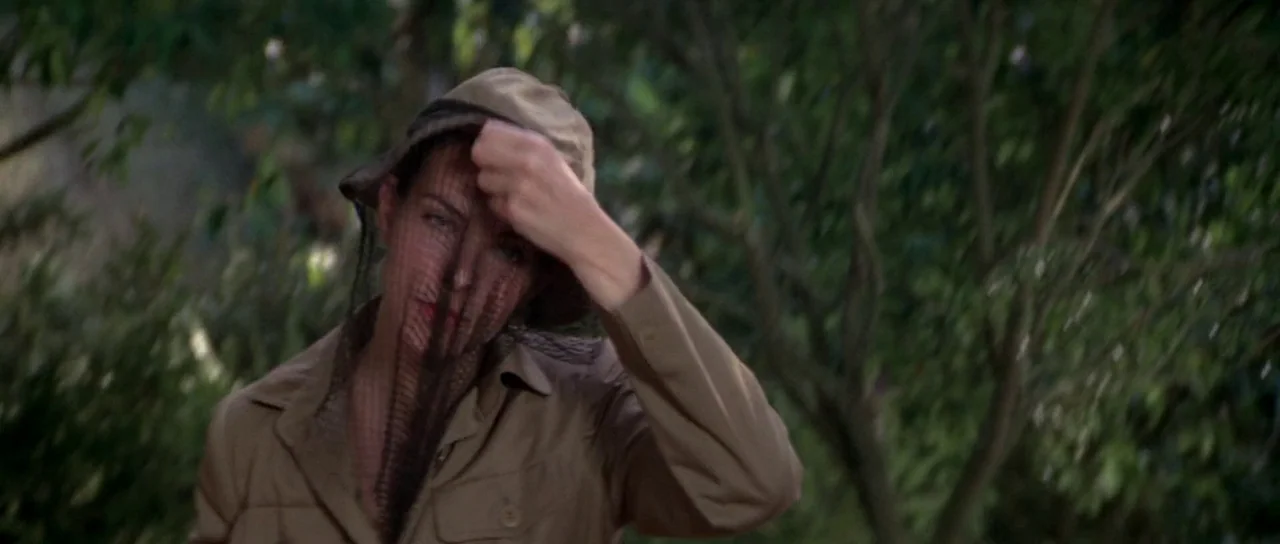 For Your Eyes Only (1981) movie still: medium — A woman stands within a dense, shadowed woodland environment with abundant green foliage. She…
