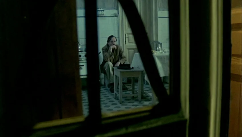 Almanac of Fall (1984) movie still: wide — An aged apartment features tiled floors and a table against a tiled back wall. A man sits at a small…