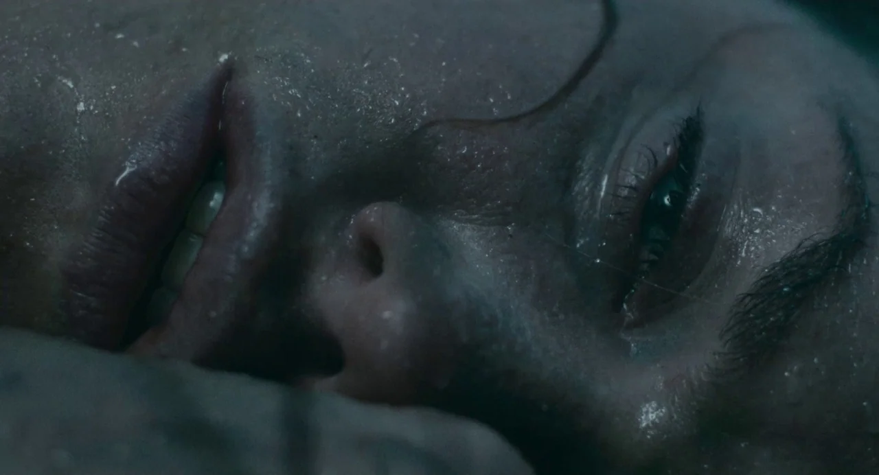 Dark River (2017) movie still: closeup — A dark space with a person's face seen in extreme close-up. The subject lies horizontally with sweat…