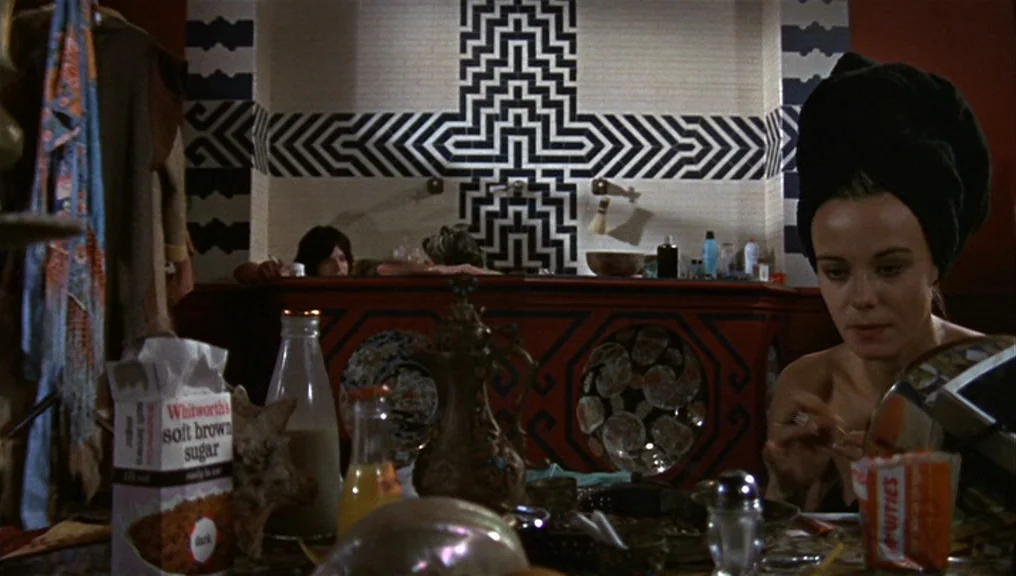 Performance (1970) movie still: medium — A tiled bathroom features a black and white geometric wall pattern above the tub. A woman sits in the…