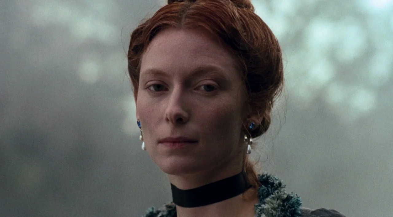 Orlando (1992) movie still: closeup — A misty, light-filled forest environment provides a blurred, desaturated background. A woman with red hair and…