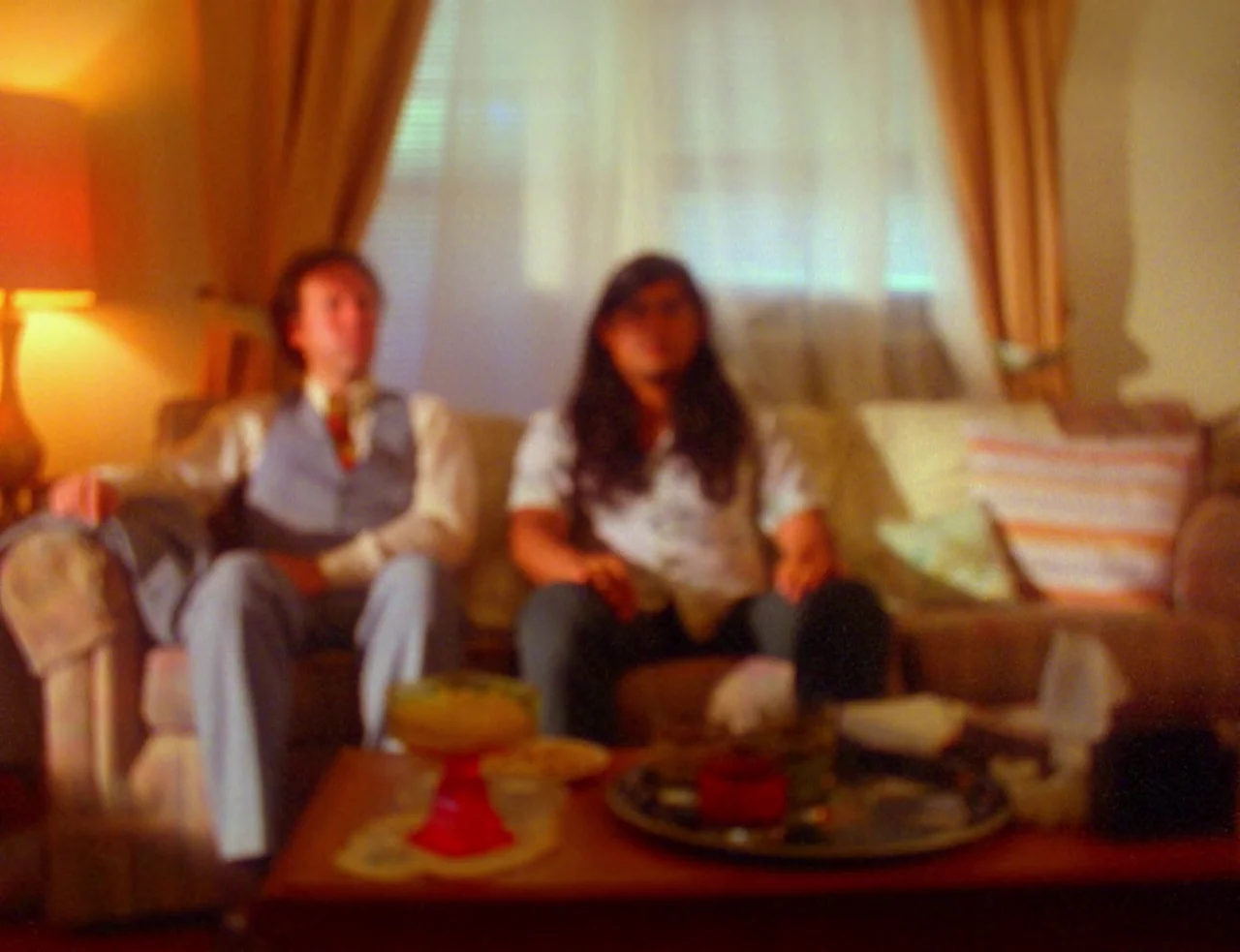 Computer Chess (2013) movie still: medium — A living room interior featuring two men sitting on a beige sofa. A wooden coffee table with…