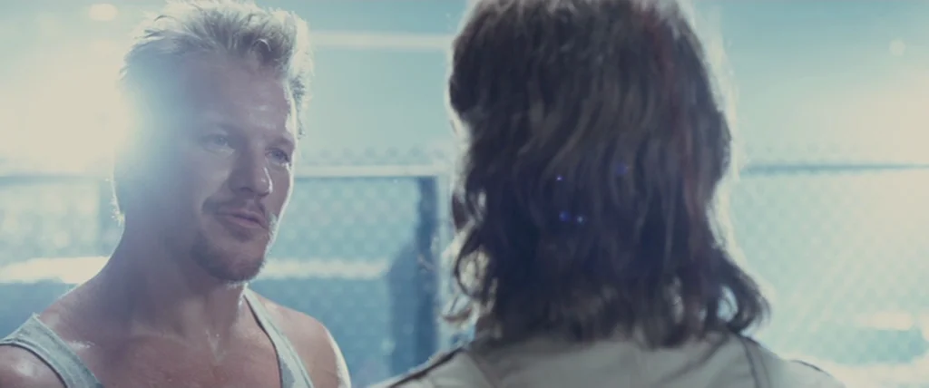 MacGruber (2010) movie still: medium — An outdoor area is enclosed by a chain link fence during bright daylight. A fair-skinned man faces another…