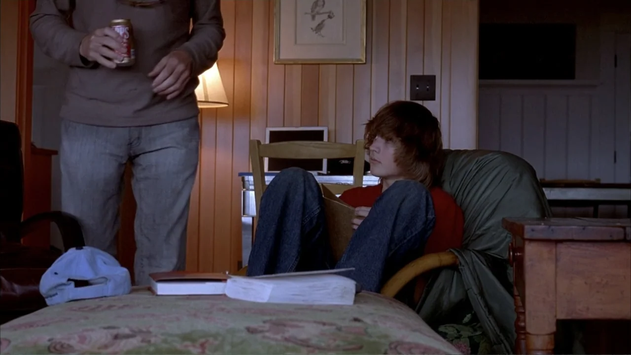 Paranoid Park (2007) movie still: medium — A living room features light wood paneling, a small table, and a desk chair. A teenage boy sits reading…