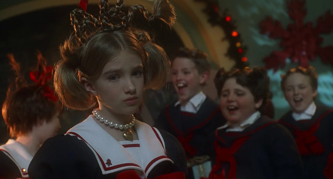 How The Grinch Stole Christmas (2000) movie still: medium — A group of children in matching sailor uniforms sing in a dim, festive environment. One…