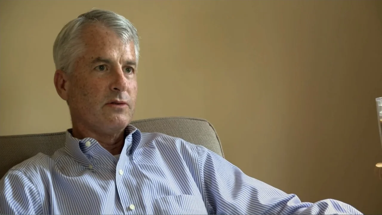 Homegrown: The Counter-Terror Dilemma (2016) movie still: medium — An indoor room with beige walls serves as the backdrop for an interview. A man in…