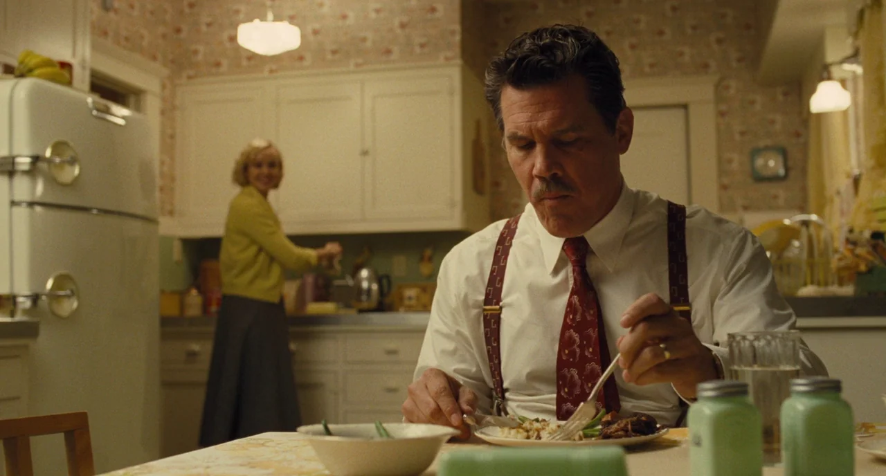 Hail, Caesar! (2016) movie still: medium — A 1950s kitchen features vintage appliances and floral wallpaper behind the subjects. A man eats at a…