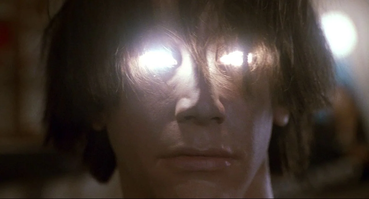 Bill and Ted’s Bogus Journey (1991) movie still: closeup — A dark indoor space contains a person with glowing bright white light in their eyes. The…