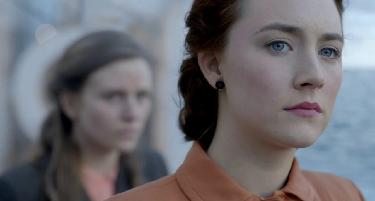 Brooklyn (2015) movie still: closeup — The deck of a ship during the day with the ocean visible in the background. A woman in the foreground looks…