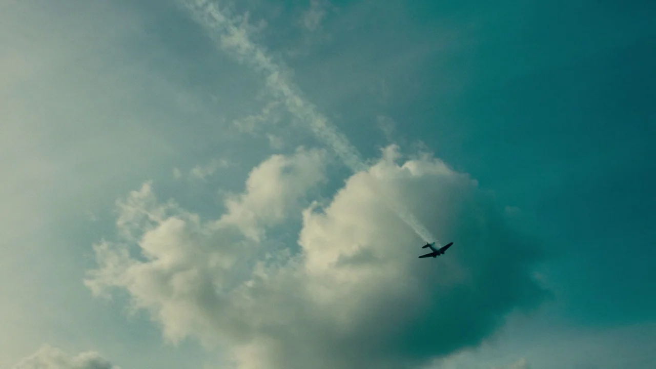 Dunkirk (2017) movie still: wide — A vast blue sky features a large, fluffy white cloud formation. A small airplane travels across the frame leaving…