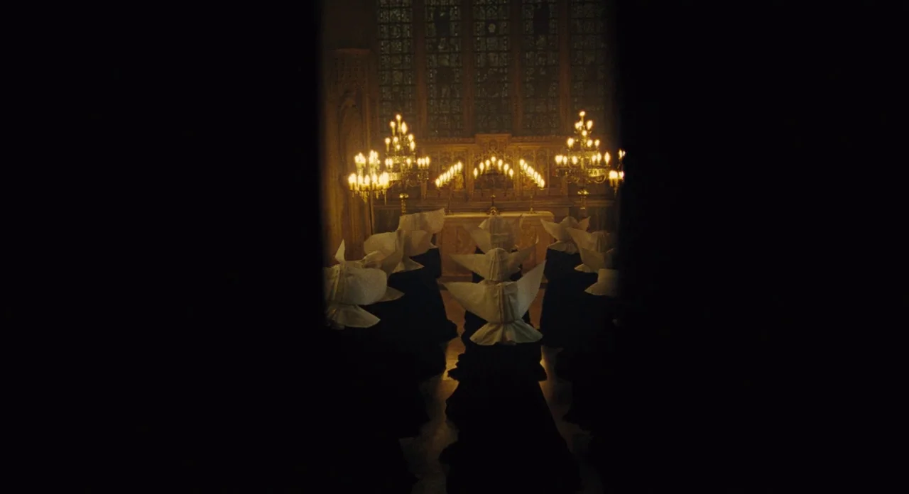 Les Misérables (2012) movie still: wide — A group of figures in dark robes and white headgear kneel inside a dim space. They face toward an altar…