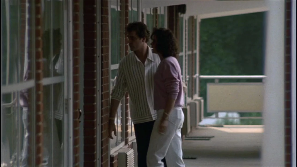 Goodfellas (1990) movie still: medium — An outdoor motel walkway features red brick walls and large glass doors. A man and a woman stand…