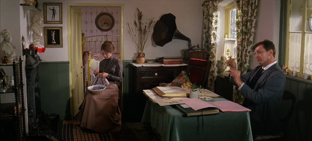 Ryan’s Daughter (1970) movie still: wide — A cozy, cluttered Victorian-style parlor features green wood paneling and floral curtains. A woman sews…