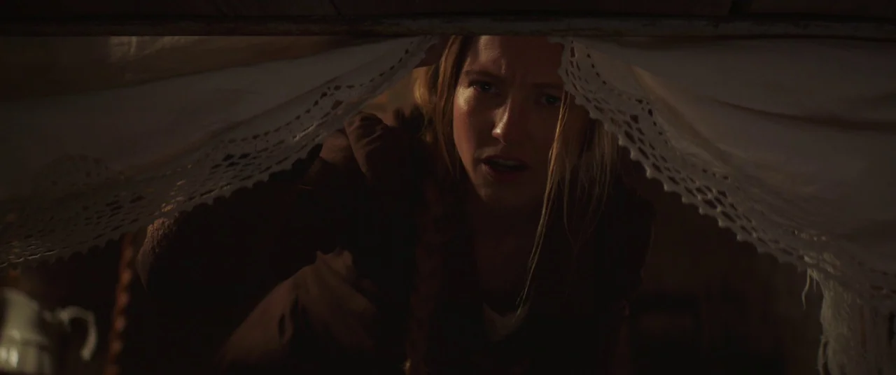 The Wind (2018) movie still: closeup — A dimly lit interior space is partially obscured by a piece of white lace fabric. A woman with blonde hair in…