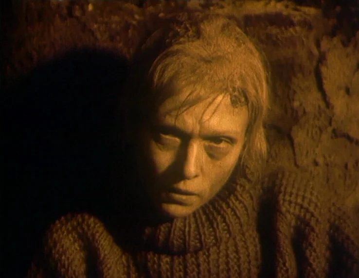 Dead Man’s Letters (1986) movie still: closeup — A dark, cramped space with textured walls surrounds a person in a thick sweater. The individual…