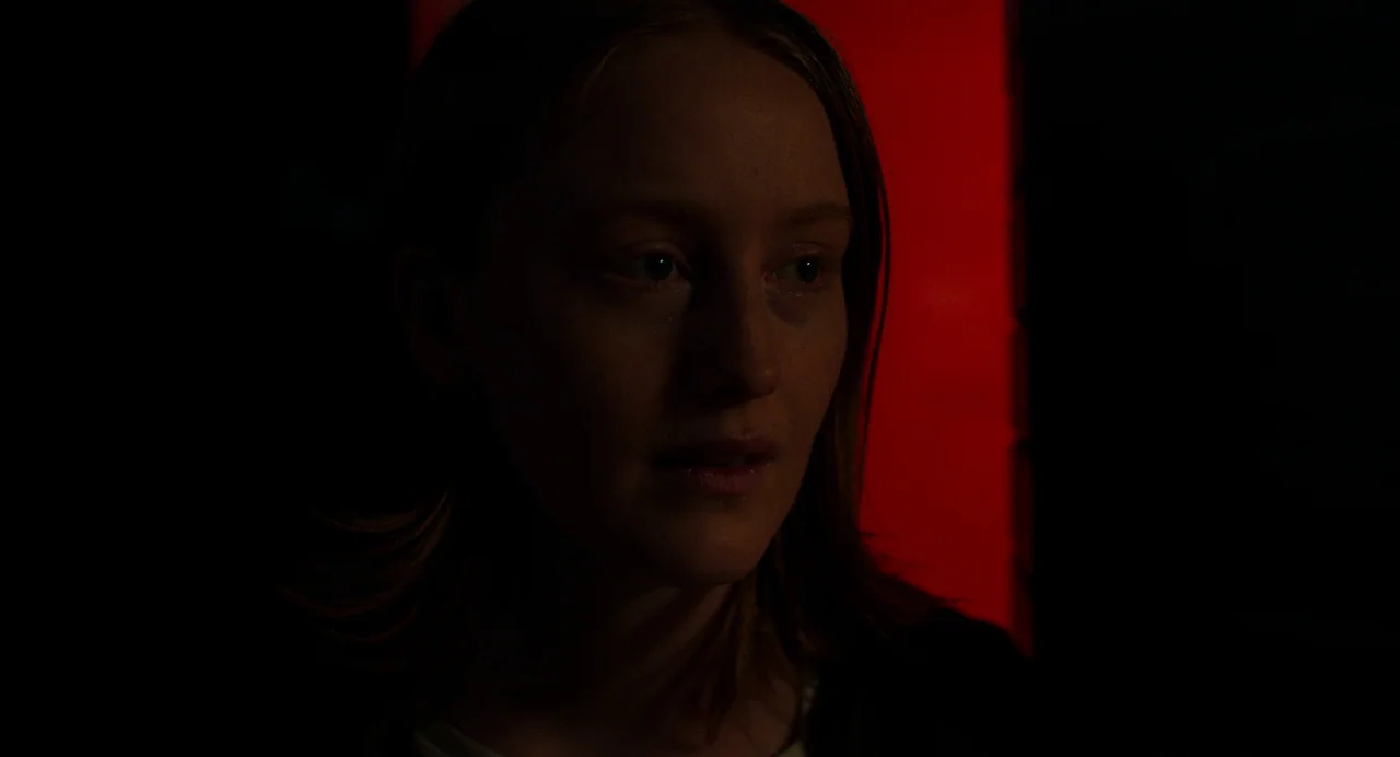 My Animal (2023) movie still: closeup — A person stands in a darkened interior with a bright red vertical light source. The subject is partially…