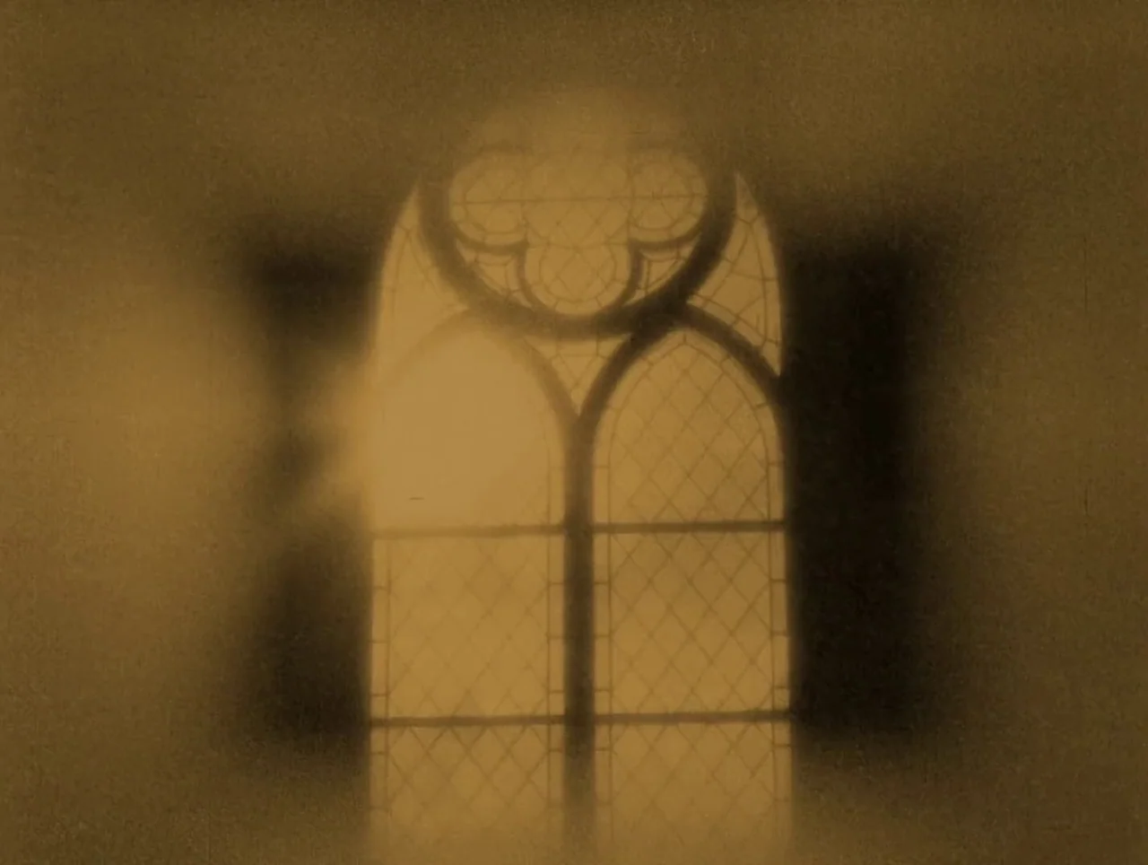 Napoleon (1927) movie still: establishing — A gothic-style arched window with ornate tracery is set into a dark wall. Light glows through the glass…