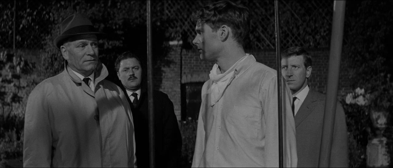 Bunny Lake Is Missing (1965) movie still: medium — Four men stand together in a dark outdoor area at night with brick walls. Three older men…