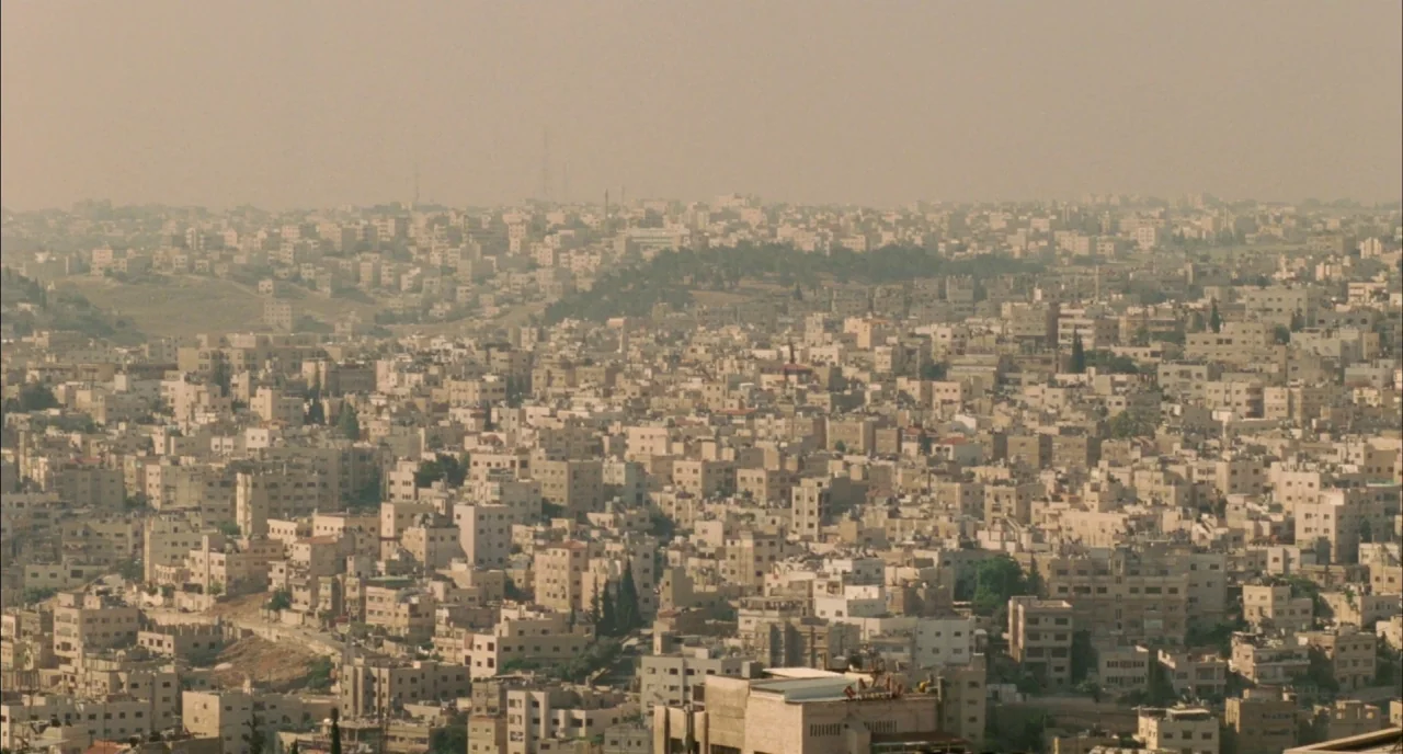 Incendies movie still: establishing — A dense urban expanse features hundreds of low-rise concrete buildings stretching toward the horizon. The…