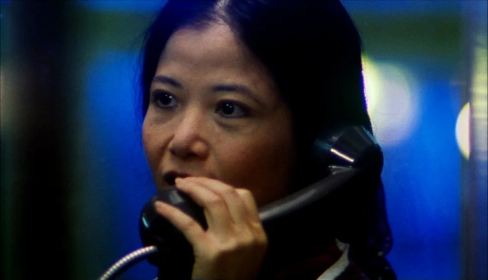Nenette et Boni (1996) movie still: closeup — An interior shot inside a cramped glass enclosure at night. A woman speaks into a black corded…